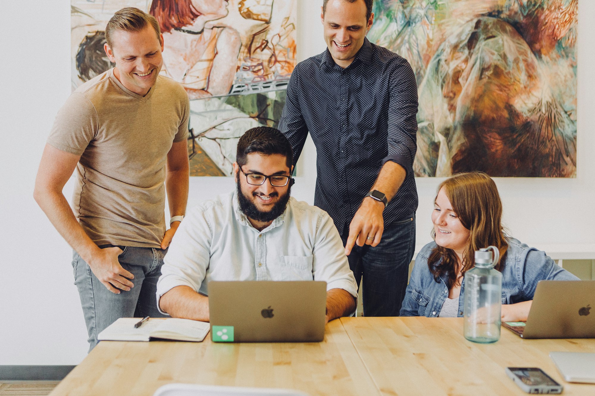 Four colleagues smiling around a laptop at a table